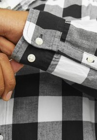 Camisa de cuadros en blanco y negro con puños abotonados, textura de tela suave y patrones contrastantes de cuadros grandes y pequeños.