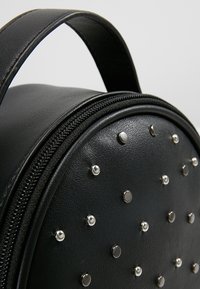 Black leather backpack with a round shape, featuring silver studs and a zipper closure. Includes a sturdy handle for carrying.