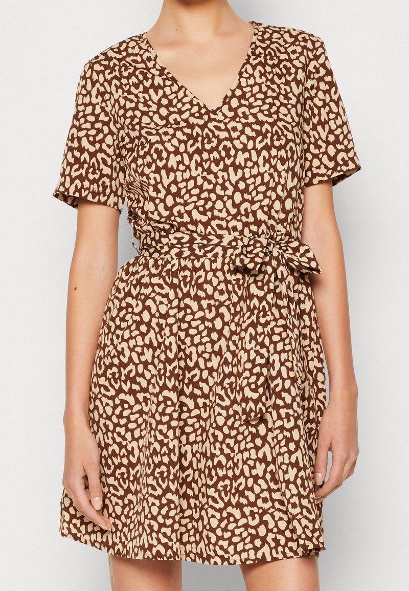 Robe à manches courtes imprimé léopard marron et beige avec encolure en V et ceinture à nouer à la taille, portée par une personne debout.
