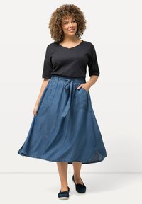 Falda en línea A de denim con bolsillos laterales, cintura con cordón y una silueta fluida. Combinada con una blusa negra de manga corta y zapatos azules.