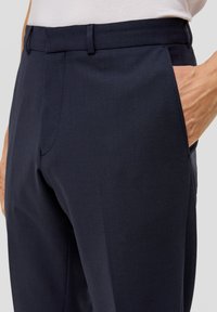 Marineblaue, maßgeschneiderte Hose mit glatter Texture, seitlichen Taschen und einem flachen Schnitt. Der Bund ist sauber verarbeitet für einen eleganten Look.