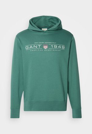 Roheline kapuutsiga dressipluus, millel on tasku, pikad varrukad ja logo trükk "GANT 1949". Valmistatud pehmest ja hingavast materjalist.