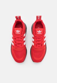 Rote Sportschuhe mit einem Mesh-Obermaterial, weißem Drei-Streifen-Design und schwarzer Gummisohle. Verfügt über eine Lasche an der Ferse für einfaches Anziehen.