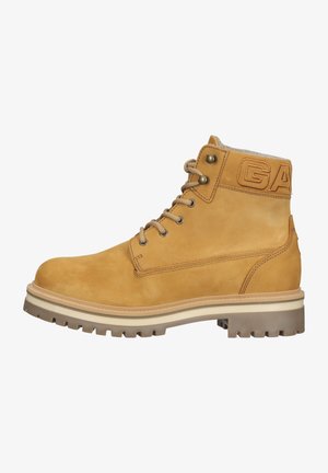 Brązowe skórzane botki za kostkę z wyściełanym kołnierzem, metalowymi oczkami i wyraźnym logo. Posiadają solidną gumową podeszwę z głębokim bieżnikiem.