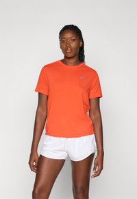 Oransje kortermet t-skjorte med rund hals og blå logo-detalj. Kombinert med hvite treningsshorts med avslappet passform og jevn tekstur.