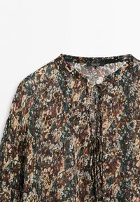 Genomskinlig blus med mångfärgat abstrakt blommönster, rund halsringning och knytning framtill.