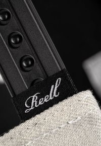 Schwarzes synthetisches Armband mit erhabenen kreisförmigen Akzenten und einem weißen Canvas-Etikett, auf dem der Markenname "Reell" in Kursivschrift abgebildet ist.