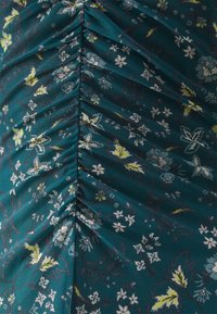Tessuto teal con motivi floreali in crema, blu e giallo. Presenta arricciature verticali lungo il centro, che aggiungono texture e profondità.