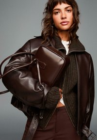 Brun læderjakke med en struktureret design, parret med en ribbet mørk sweater og en matchende brun crossbody taske. Simpel hardware accent.