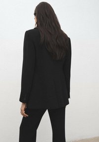 Czarna, dopasowana marynarka o strukturalnej sylwetce z zapięciem na jeden guzik, wykonana z gładkiego materiału, z długimi rękawami.