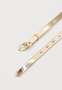 Kiiltävä kullanvärinen nahkavyö, jossa on ovaalinmuotoinen solki ja geometrinen kuvio. Kuvassa näkyy solki ja säädettävät reiät yksivärisellä taustalla.