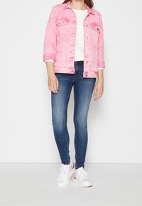 Giacca di jeans rosa con una texture sbiadita e due tasche sul petto, abbinata a jeans blue slim fit e sneakers bianche con dettagli rosa.