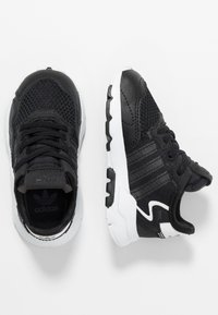 Chaussures de sport noires avec dessus en mesh, accents en cuir noir texturé, semelle intermédiaire blanche, semelle extérieure noire et trois bandes caractéristiques sur les côtés.