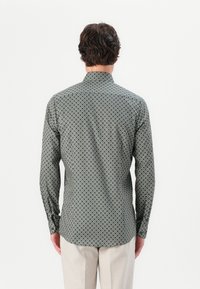 Hemd mit Knopfleiste aus gemustertem Stoff; dunkelgrün mit kreisförmigen weißen und blauen Designs; lange Ärmel, gerader Kragen und abgerundeter Saum.