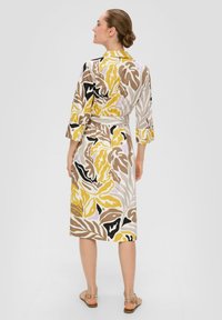 Robe portefeuille à motifs floraux dans des teintes jaunes, noires et brunes. Fabriquée en tissu léger, elle possède des manches trois-quarts et une ceinture à nouer.