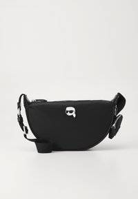 Bolso de hombro negro de nylon con forma curvada, que cuenta con un cierre de cremallera, correa ajustable y un notable logo elevado en la parte frontal.