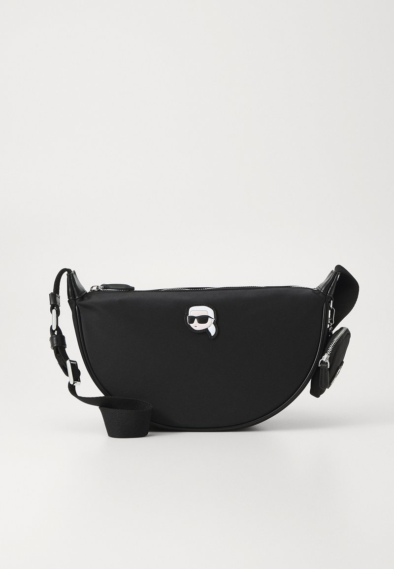 Bolso de hombro negro de nylon con forma curvada, que cuenta con un cierre de cremallera, correa ajustable y un notable logo elevado en la parte frontal.
