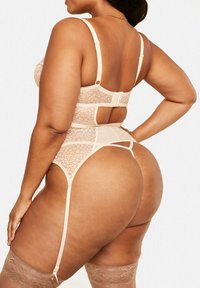 Bodysuit en dentelle nude, avec des bretelles réglables, des textures transparentes et un dos découpé. Inclus des jarretelles et des bas attachés.