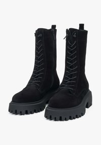 Czarne zamszowe buty wojskowe na grubej gumowej podeszwie, z przodu sznurowane, z bocznym zamkiem błyskawicznym dla łatwego zakładania. Teksturowane wykończenie.