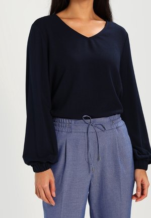 Granatowy, długi rękaw top z dekoltem w serek i bufiastymi rękawami, w połączeniu z jasnoniebieskimi wzorzystymi spodniami z regulowanym sznurkiem w pasie.