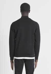 Sudadera negra con cuello alto, mangas raglán y dobladillo de canalé. El material parece suave y texturizado. Camiseta blanca visible en la parte inferior.