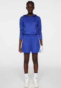 Kuningan biru kerajaan dengan tali serut, dipadukan dengan celana pendek yang serasi. Memiliki logo di dada, lengan setengah panjang, dan tekstur kain yang halus.