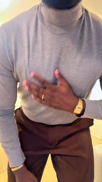 Grå polotröja, figursydd med ribbad halsringning, kombinerad med mörkbruna byxor. Guldklocka på vänster handled, händer delvis synliga.