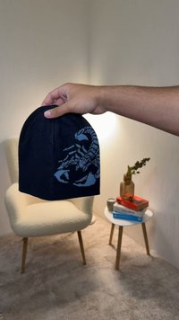 Svart stickad mössa med en skorpiondesign i blått med röda detaljer. Mössan har en rund topp och en åtsittande passform.