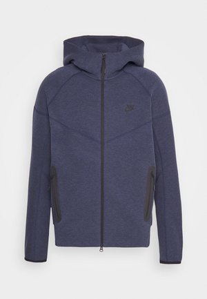 Dunkelblauer Kapuzenpullover mit Reißverschluss und gefütterter Kapuze, ausgestattet mit einem schwarzen Logo, zwei Seitentaschen und kontrastierenden grauen Akzenten an den Nähten.