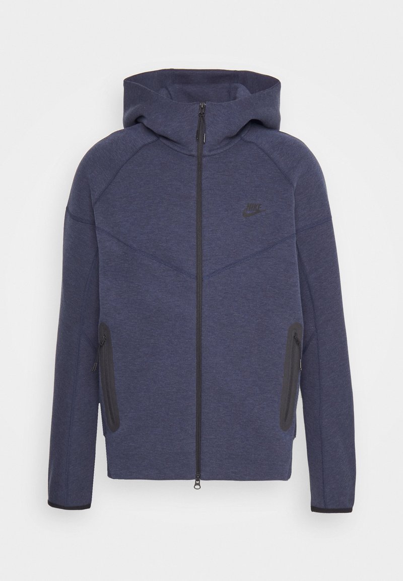 Sweat à capuche zippé bleu marine avec une capuche doublée, arborant un logo noir, deux poches latérales et des accents gris contrastants sur les coutures.