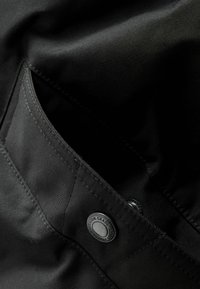 Schwarze Stofftasche mit silbernem Druckknopf, mit glatter Textur und sauberer Naht, Teil eines strukturierten Designs.