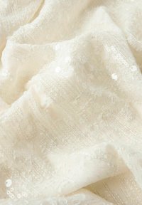 Valge kangas keeruka tekstuuriga, mis sisaldab sädelevateid ja õmmeldud mustreid. Pehme ja kerge, ühtlase läikega kogu pinnal.