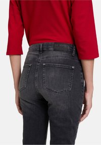 Šedé džíny z denimu s středním pasem, zadními kapsami a koženou značkou. Tkanina vykazuje jemnou texturu a mírně vybledlý vzhled.