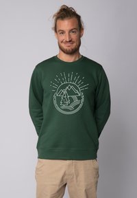 Sweat à capuche vert avec un graphique rond représentant des montagnes et un arbre. Texture douce, col rond et manches longues. Coupe décontractée.