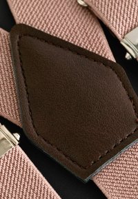 Bretelles ajustables en tissu rose avec des accents en cuir marron. Présente des clips en métal argenté et une surface texturée.