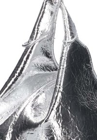 Zilveren metallic tote bag met een gekreukeld oppervlak. Voorzien van dubbele handvatten en een open top ontwerp, wat de glanzende afwerking en unieke uitstraling benadrukt.