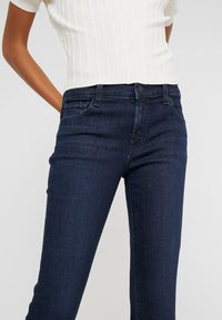 Jeans de corte slim en azul oscuro, con una textura suave, que cuentan con un cierre de botón, cinco bolsillos y detalles de costura sutiles.