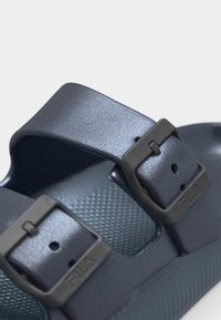 Σκούρα γκρι σαγιονάρα με δύο ρυθμιζόμενους ιμάντες που διαθέτουν μαύρες αγκράφες σε υφασμένο πέλμα.