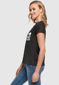 Sort bomulds t-shirt med korte ærmer, der har hvid tekst på fronten. Løs pasform, rund halsudskæring og en glat tekstur.