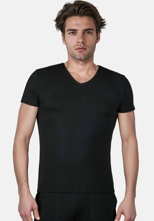 Young man with short brown hair wearing a fitted black V-neck short sleeve T-shirt standing against a plain light background.