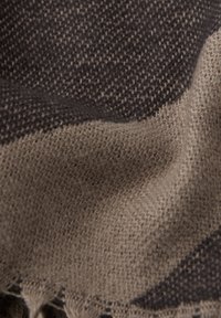 Tissu tissé aux tons terreux de brun et beige, présentant une surface texturée avec un motif subtil et des bords frangés.