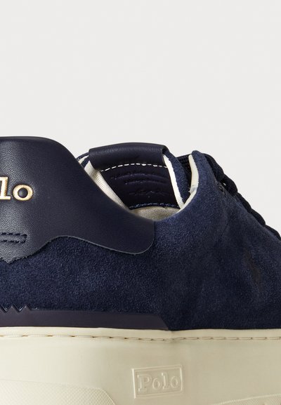 Tengerészkék velúr sneaker bőrkivitelű részletekkel, fehér gumitalppal és arany logóval a hátsó részen, texturált felső résszel és fűződizájnnal.