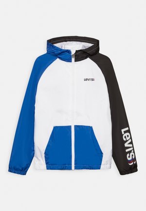 Kurtka przeciwwietrzna z kapturem, białym przodem, niebieskim lewym rękawem i kieszeniami, czarnym prawym rękawem z logo Levi's na rękawie i piersi.