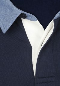 Poloshirt mit einem navyblauen, gerippten Körper, kontrastierendem Chambray-Kragen und weißem Innenfutter am Halsausschnitt. Sichtbares schwarzes Knopfdetail.