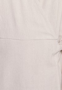 Tejido de color beige claro con una superficie texturizada. Presenta una costura diagonal y un acento anudado. Material suave y elástico con un acabado liso.