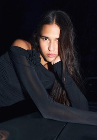 Czarna bluzka odkrywająca ramiona z przezroczystymi, długimi rękawami, ozdobiona teksturowanym kwiatowym akcentem na ramieniu oraz marszczonym detalem z tkaniny.