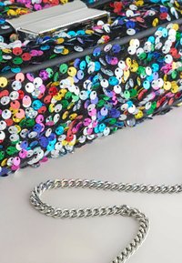 En liten svart väska täckt av multikolorade paljetter med en silverkedja som axelrem och ett glänsande lås på toppen.