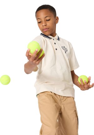 Αγόρι που φοράει πόλο με θέμα το τένις, ζογκλερικά με τρεις κίτρινες μπάλες του τένις σε λευκό φόντο.