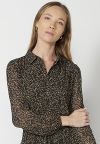 Blusa nera a fiori con collo classico, maniche lunghe trasparenti e chiusura a bottone con un delicato motivo floreale multicolore.
