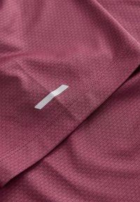 Bordowy materiał sportowy z teksturowanym wzorem diamentowym. Zawiera małe metaliczne logo oraz widoczne detale szwów.